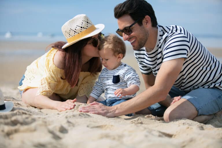 A couple and a child play in the sand on a sunny beach, all wearing casual summer clothes and sunglasses, enjoying carefree moments reminiscent of the security offered by revocable trusts for families.