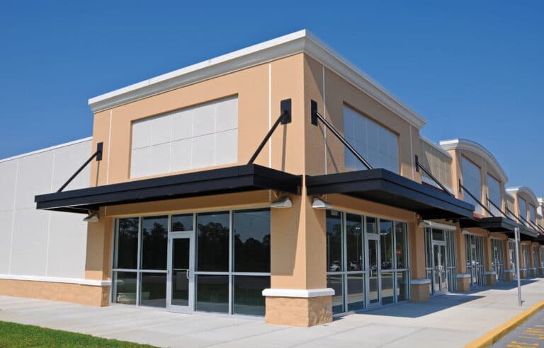 A modern, empty strip mall with large glass windows stands silently under a clear blue sky, its spaces hinting at the aftermath of recent commercial evictions in Florida.