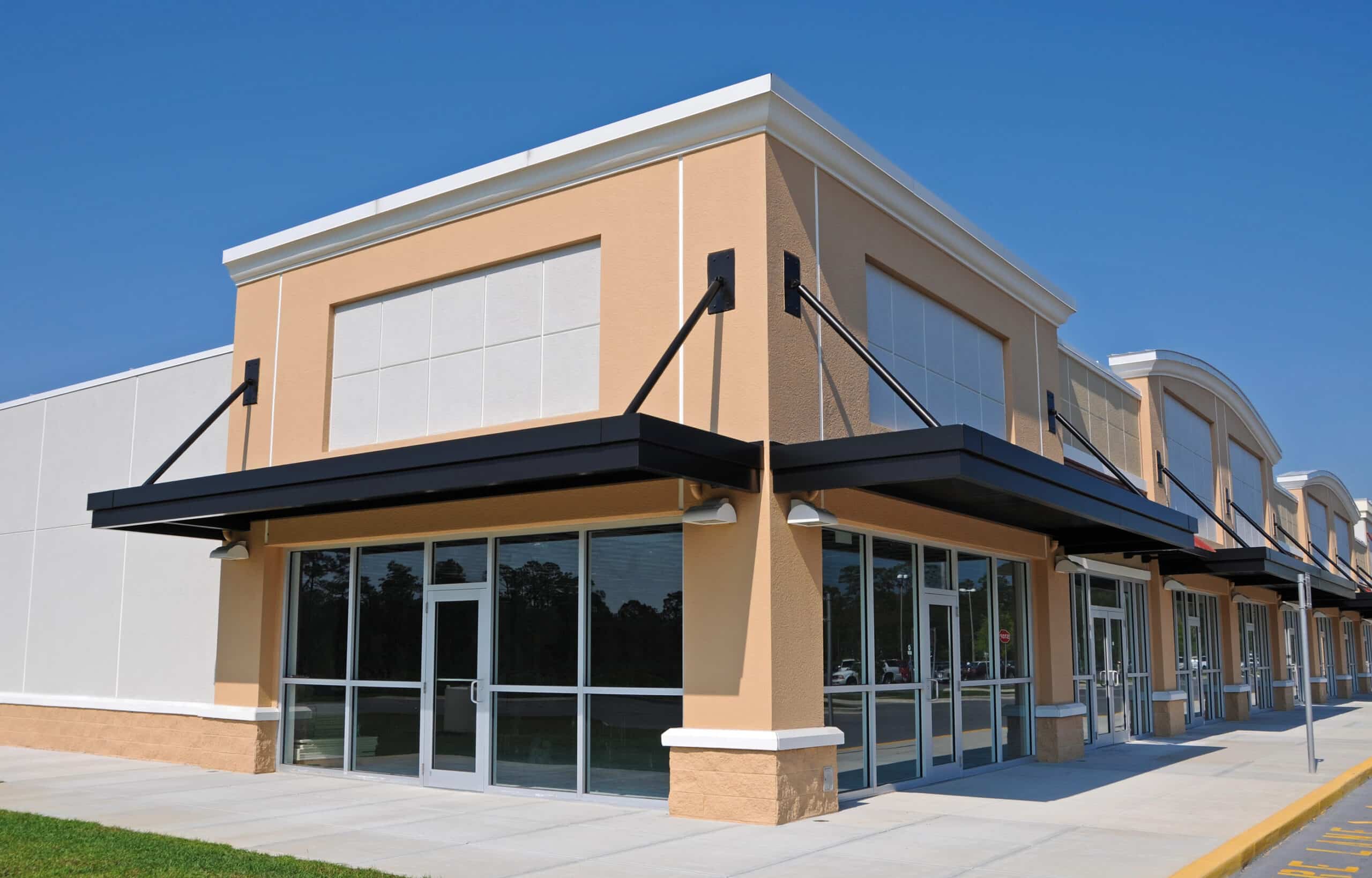 A modern, empty strip mall with large glass windows stands silently under a clear blue sky, its spaces hinting at the aftermath of recent commercial evictions in Florida.