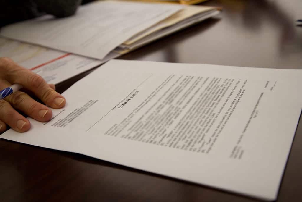 A hand holds a pen near a document titled Deed on Trust surrounded by papers detailing estate plans and traditional wills, neatly spread across the table.